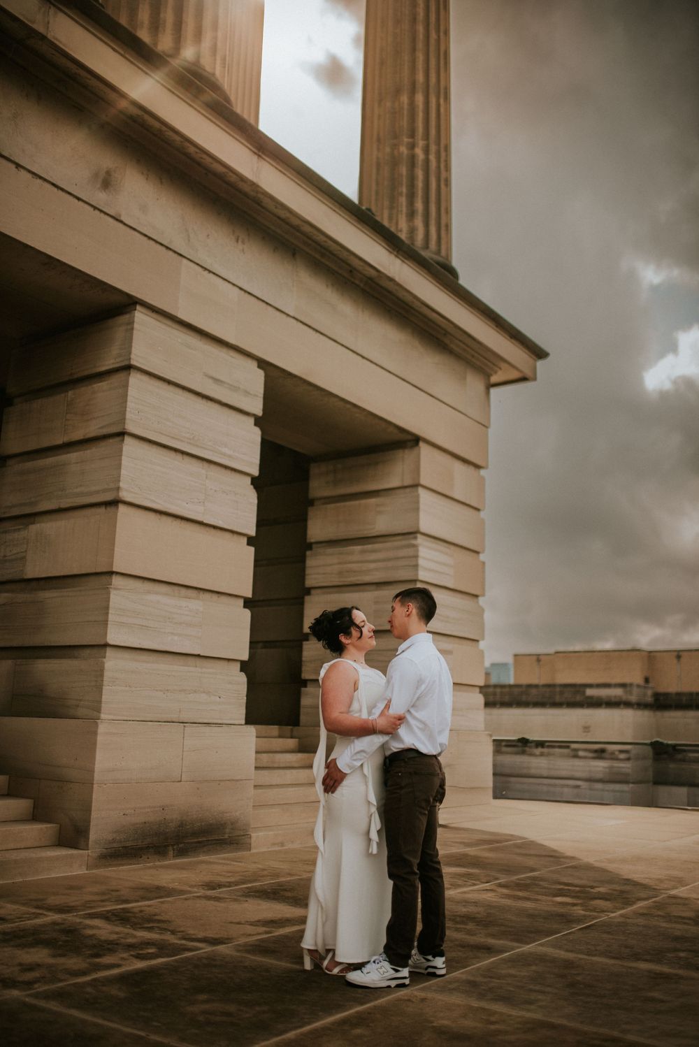 Engaged couple outside a historical building holding each other with sunlight peeking through the clouds in Nashville, Tennessee.