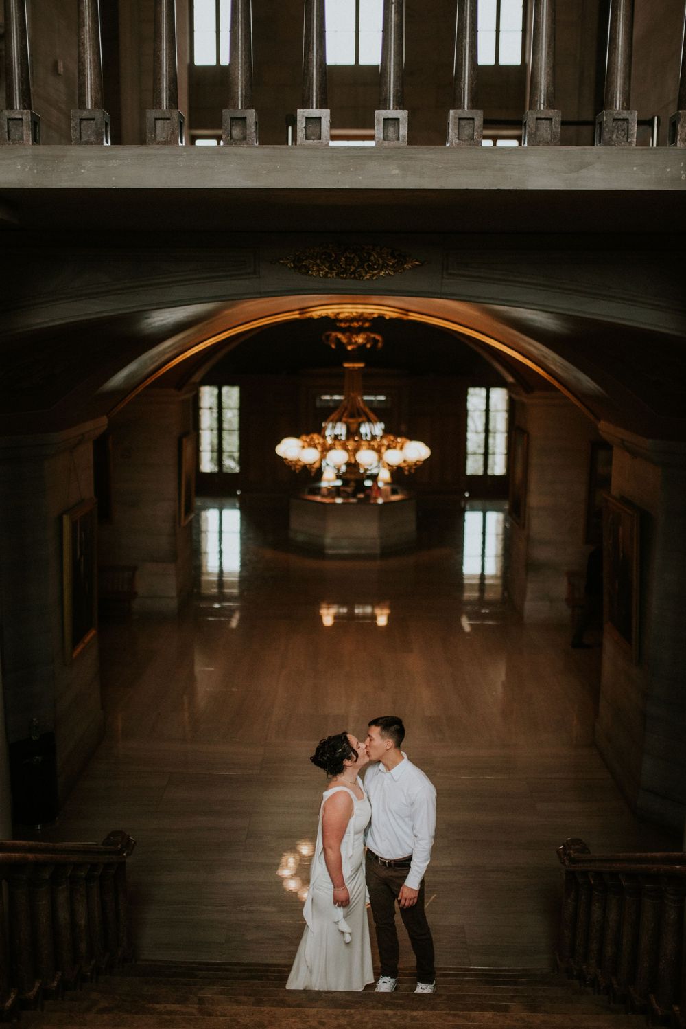 Luxury couple stands at the bottom of the stairs of a historic building kissing as their affordable photographer takes a photo.