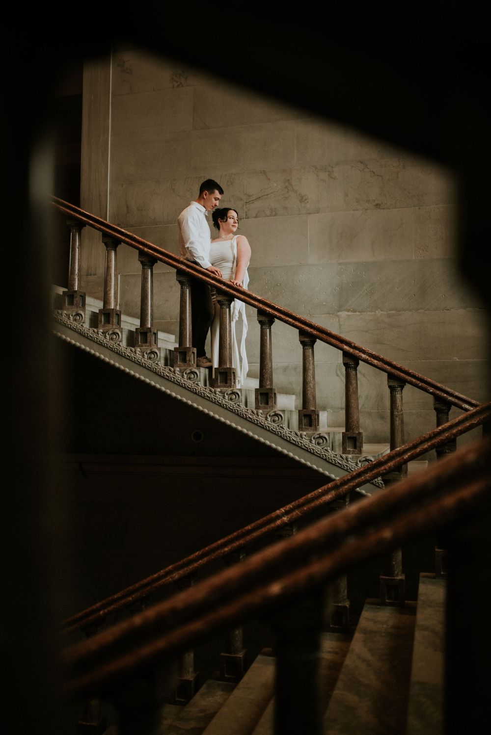 Framed within the staircase railing, an engaged couple stares off into the natural light coming from the window.