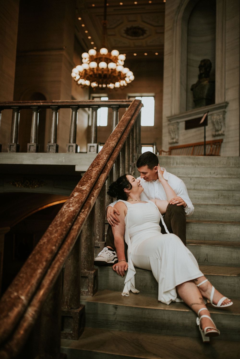 Engaged couple sit on the stairs in Nashville TN as they look at each other in a historic building.