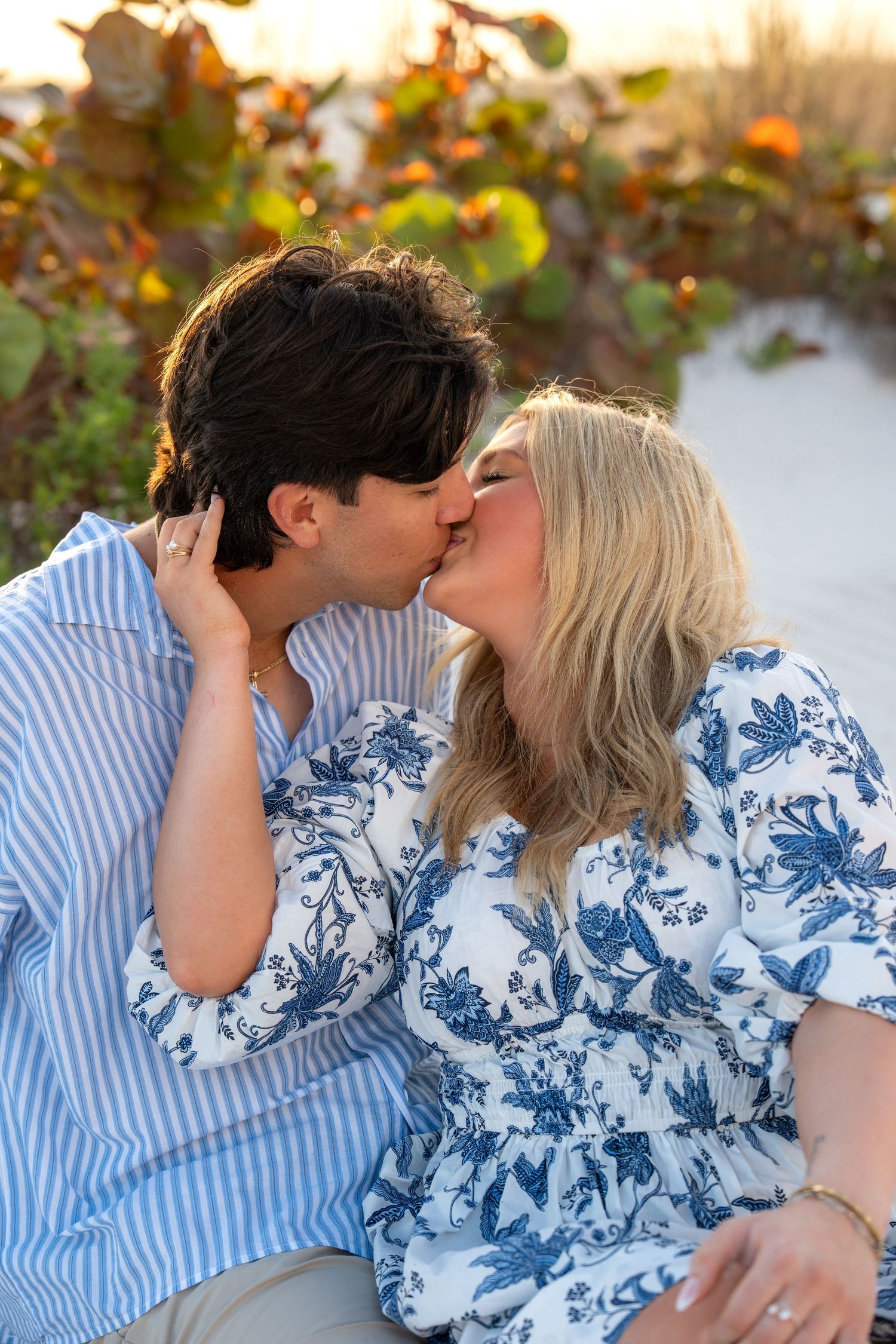 Couple sharing a passionate kiss on a white sand beach with warm sunset light behind them.