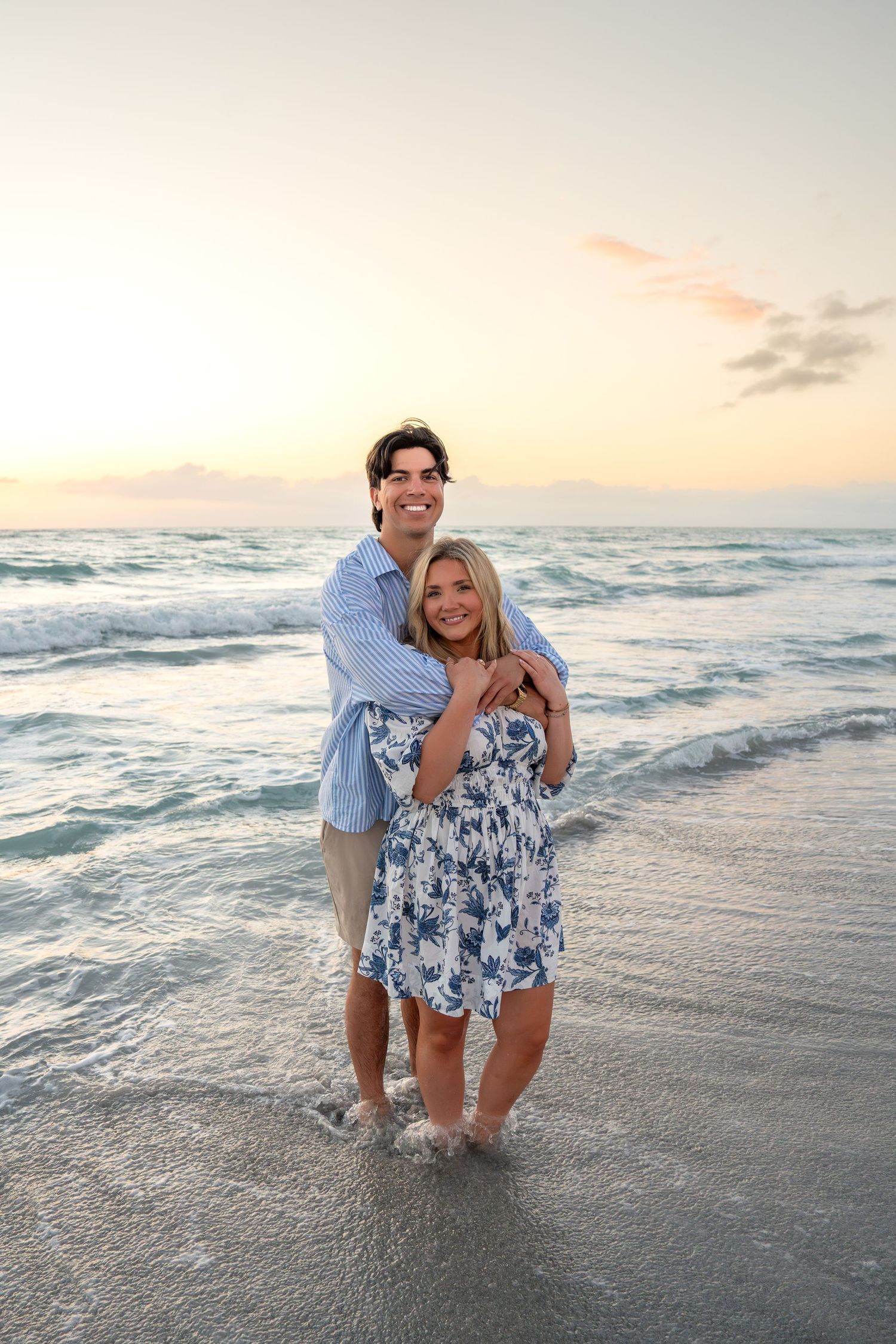 Happy couple hugging at the beach during sunset, standing in shallow ocean water.