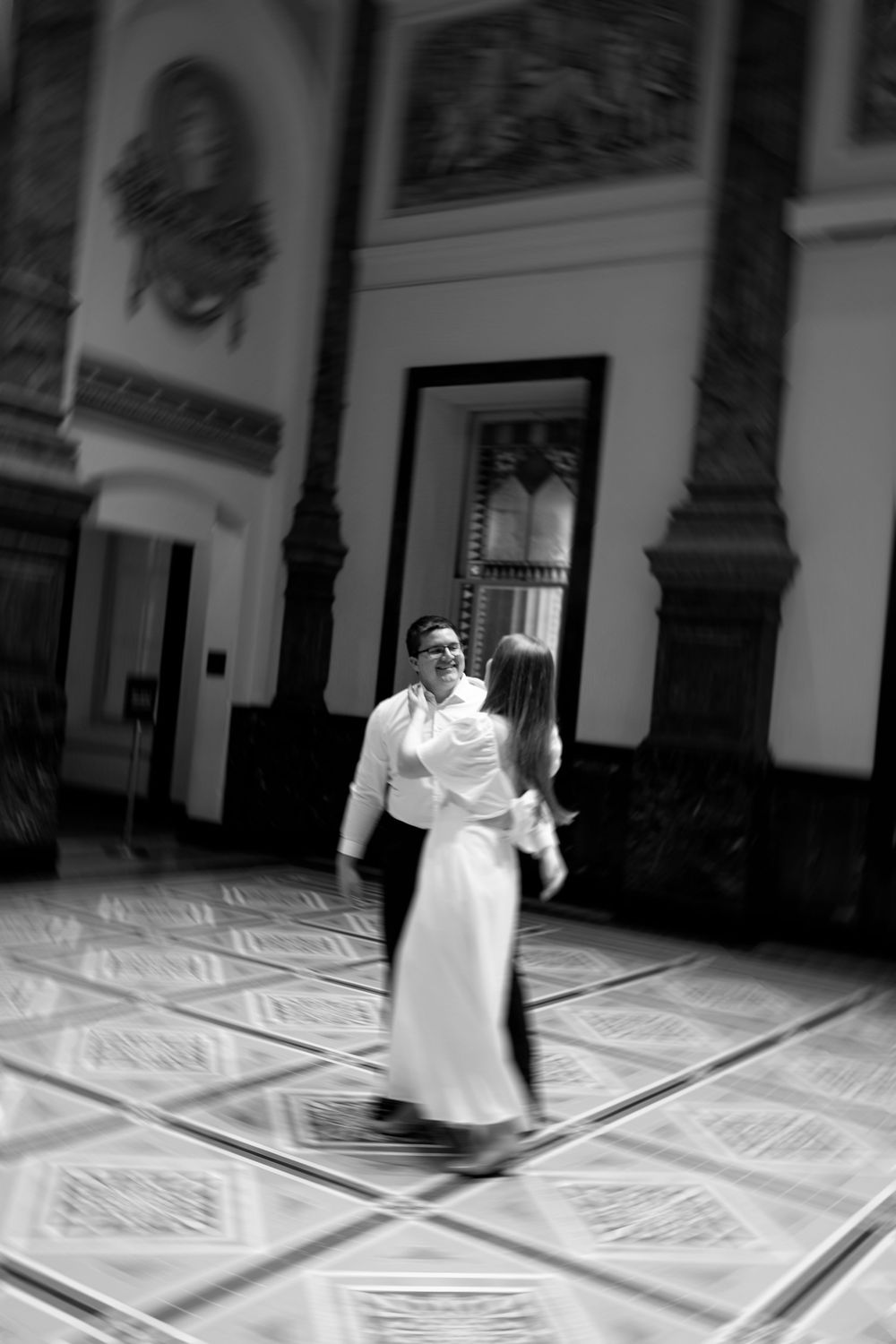 Blurred artistic black and white photo of couple dancing in ornate historic building interior.