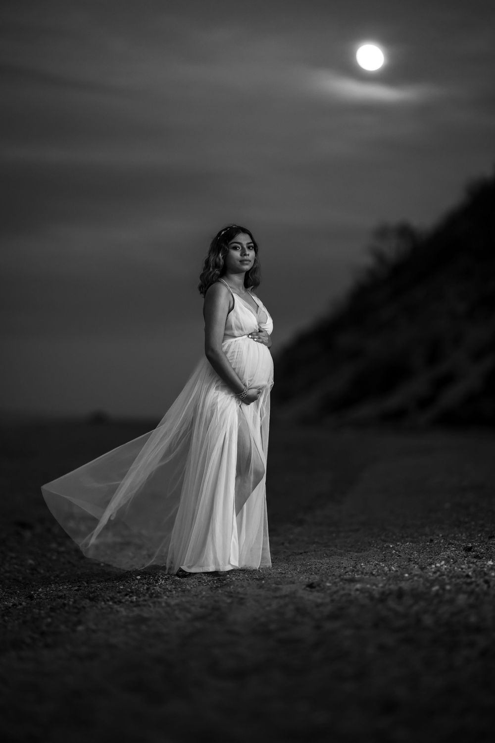 A dramatic black and white series of photos showing a figure in a flowing white dress posing on a beach at moonlight.