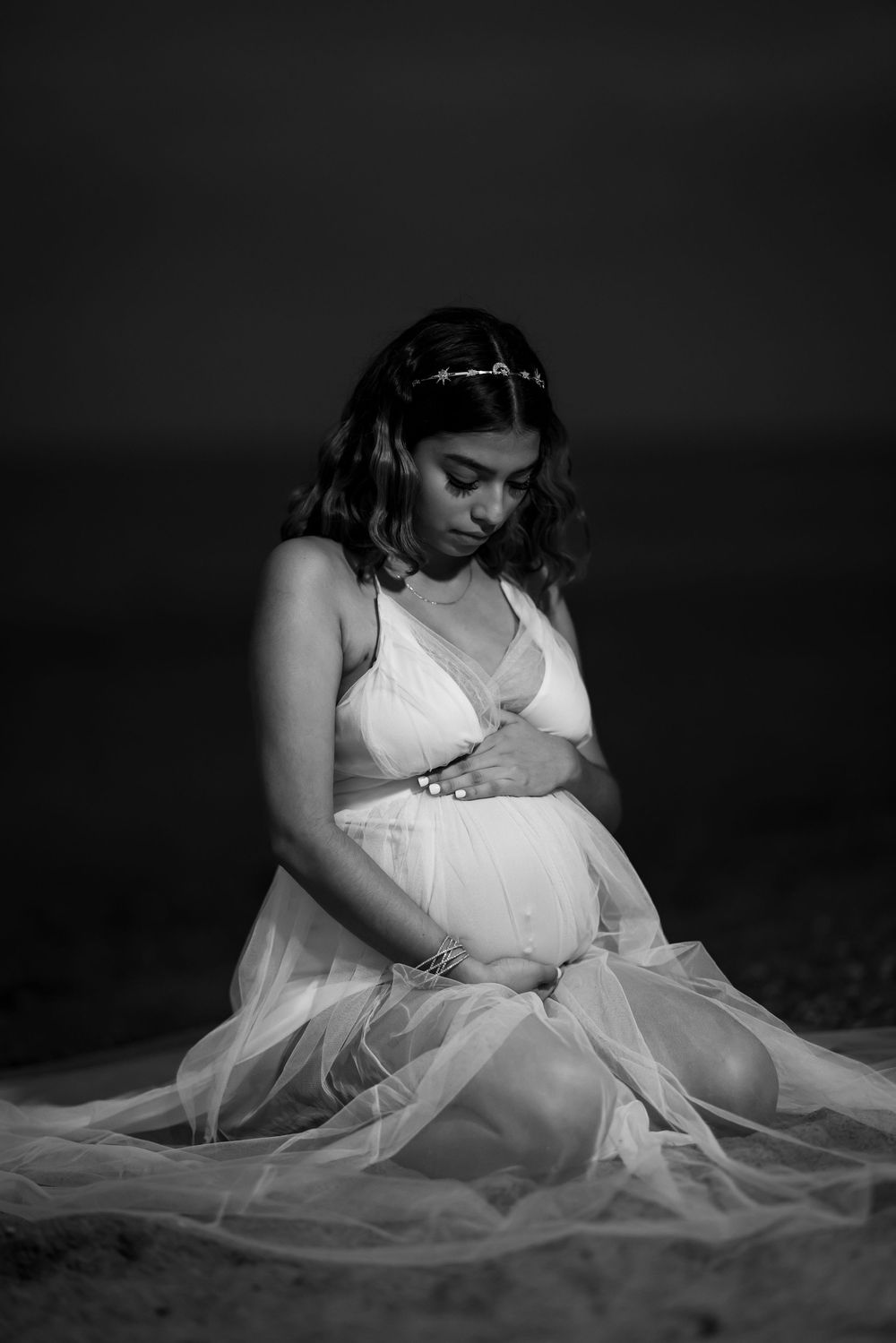 A series of black and white photos showing a figure in a white dress with flowing tulle fabric sitting on the ground.