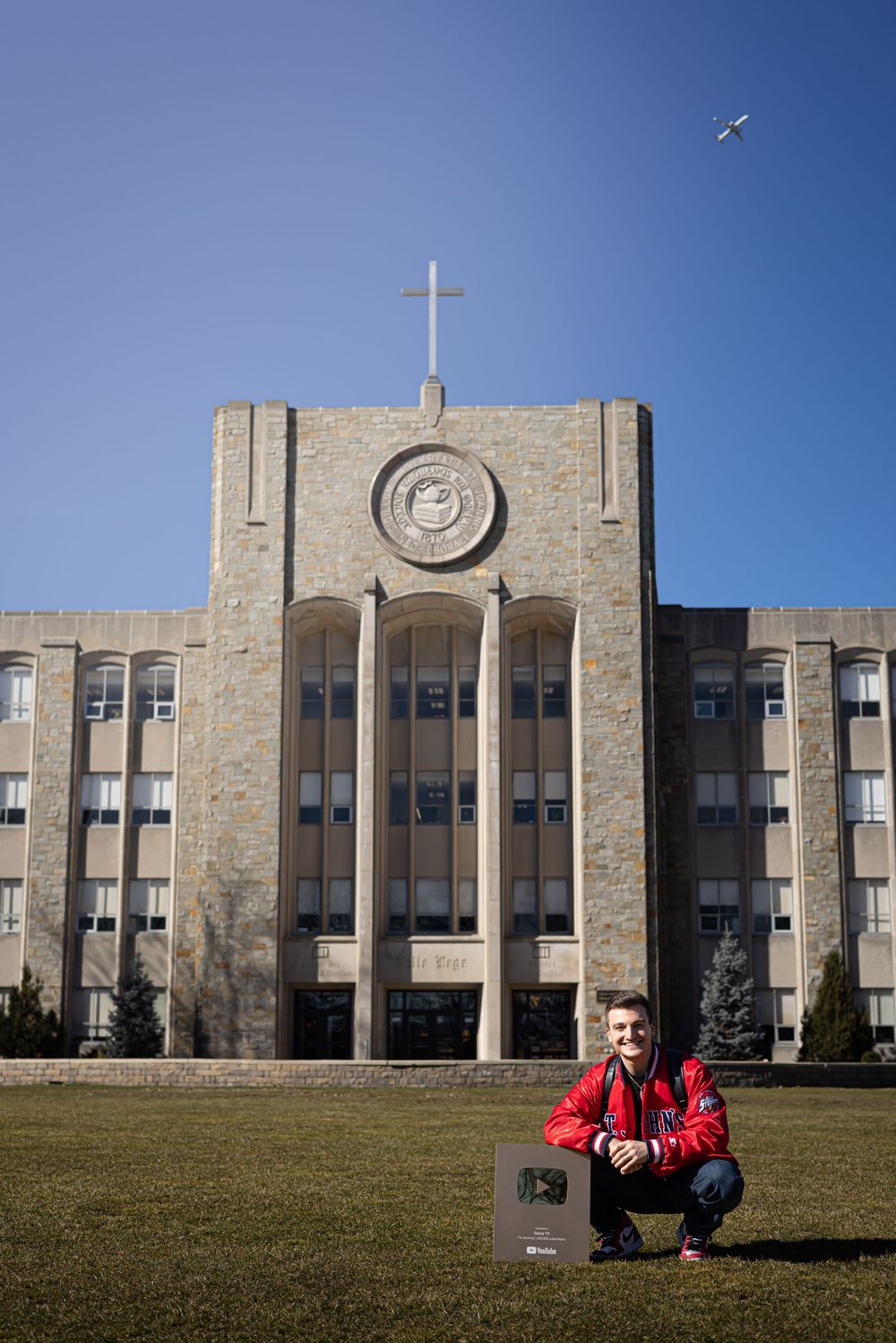 Stone facade of an Art Deco style academic building with a cross on top against blue sky.