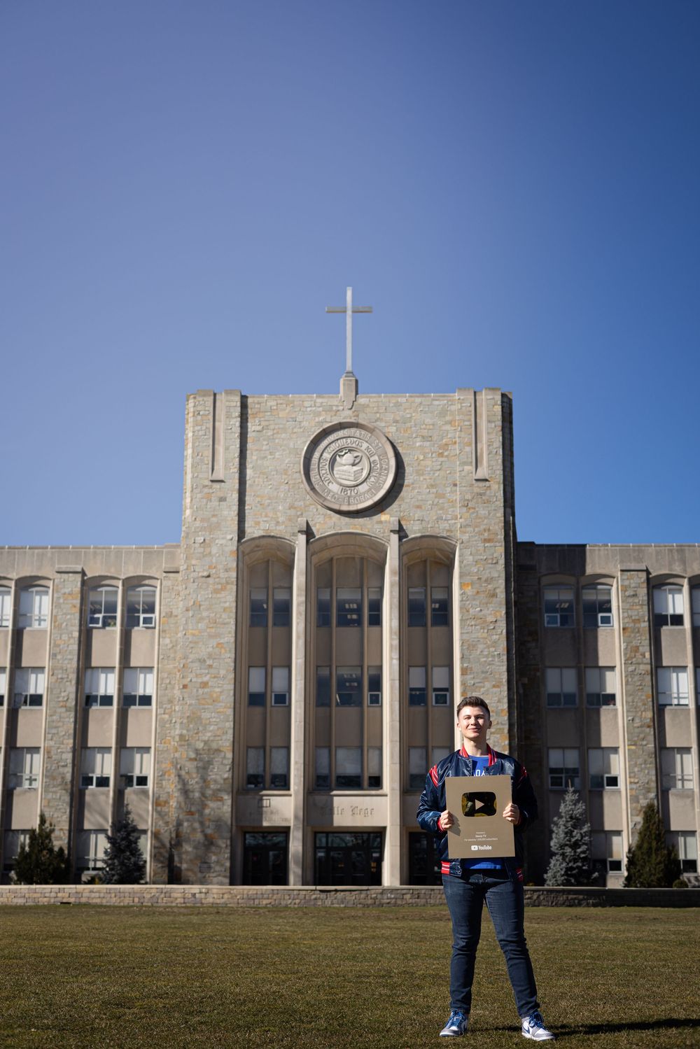 A large stone building with Gothic architecture and a cross on top stands against a bright blue sky.