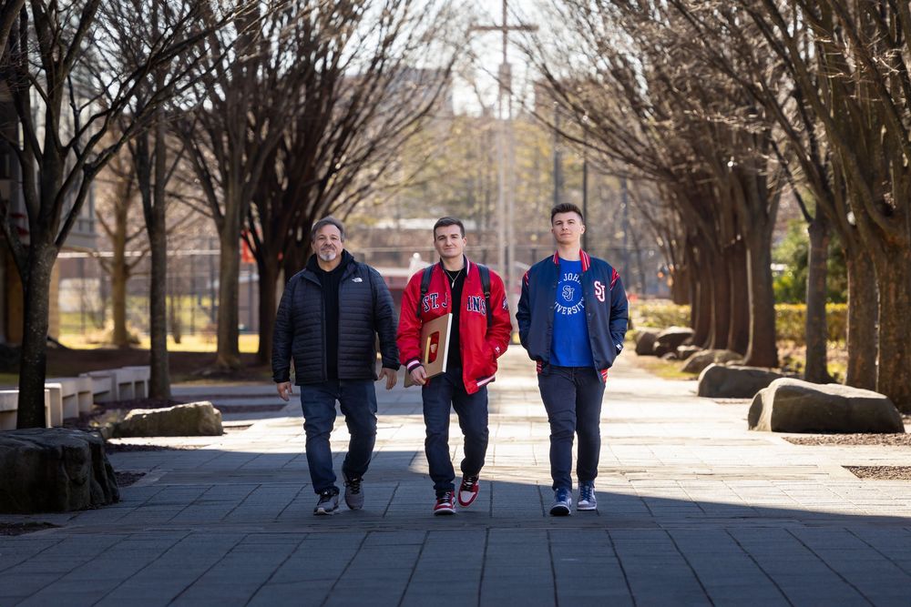 Group walking along tree-lined pathway outside stone building on sunny winter day.
