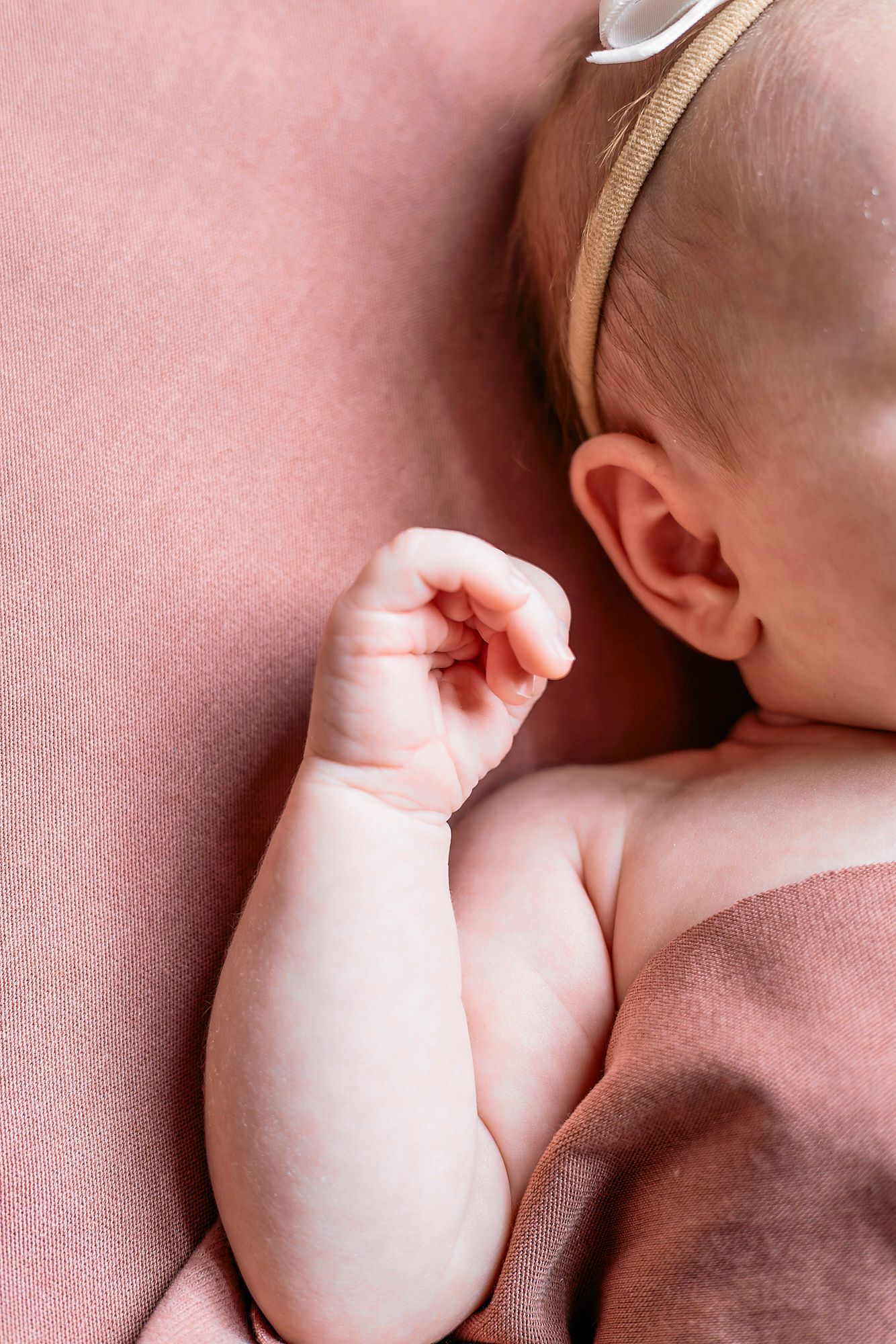 Close-up view of a newborn baby breastfeeding while lying on a pink blanket or surface.