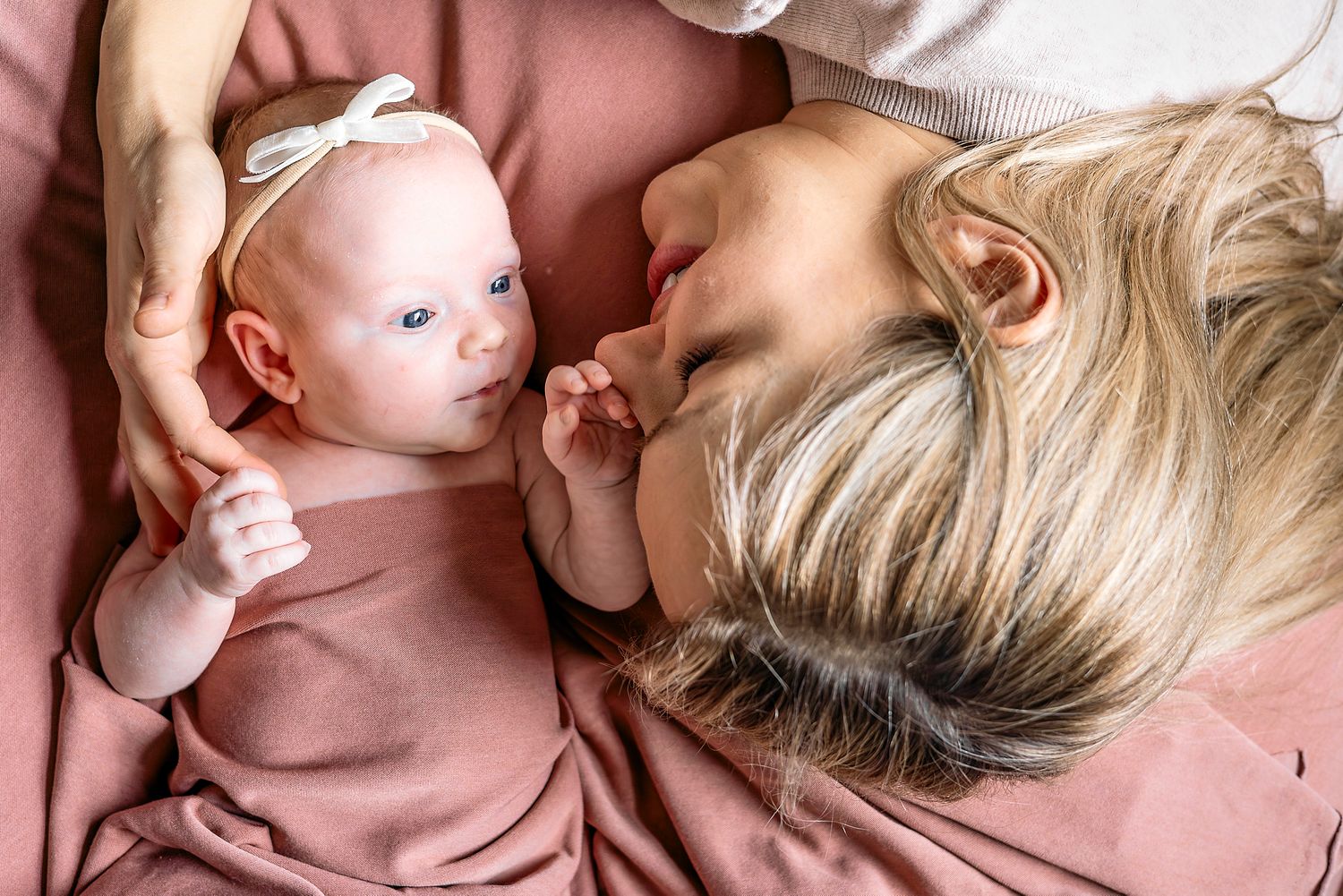 A tender moment between parent and baby lying on pink fabric, sharing a close connection.