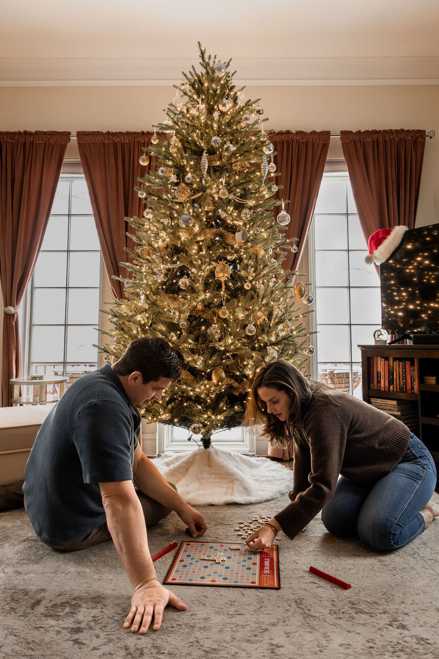 A sequence showing someone crawling across a carpeted floor to plug in Christmas tree lights near a decorated evergreen tree.