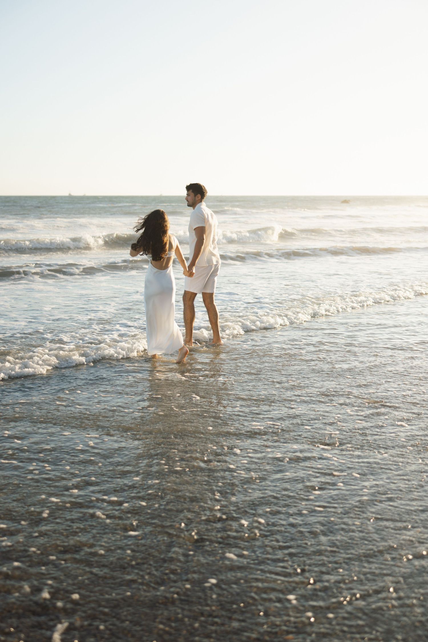 Malibu engagement session at El Matador with a couple holding hands in the waves and looking out at the ocean