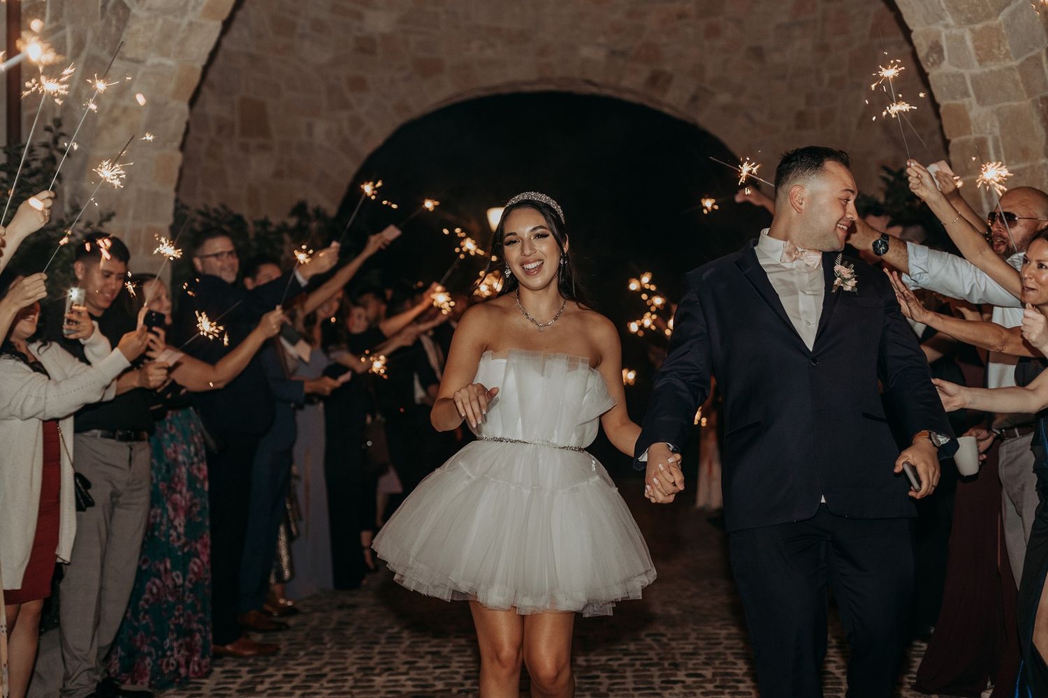 Bride and groom exit wedding reception through sparkler tunnel with smiling guests celebrating at night at The Havens Country Club.