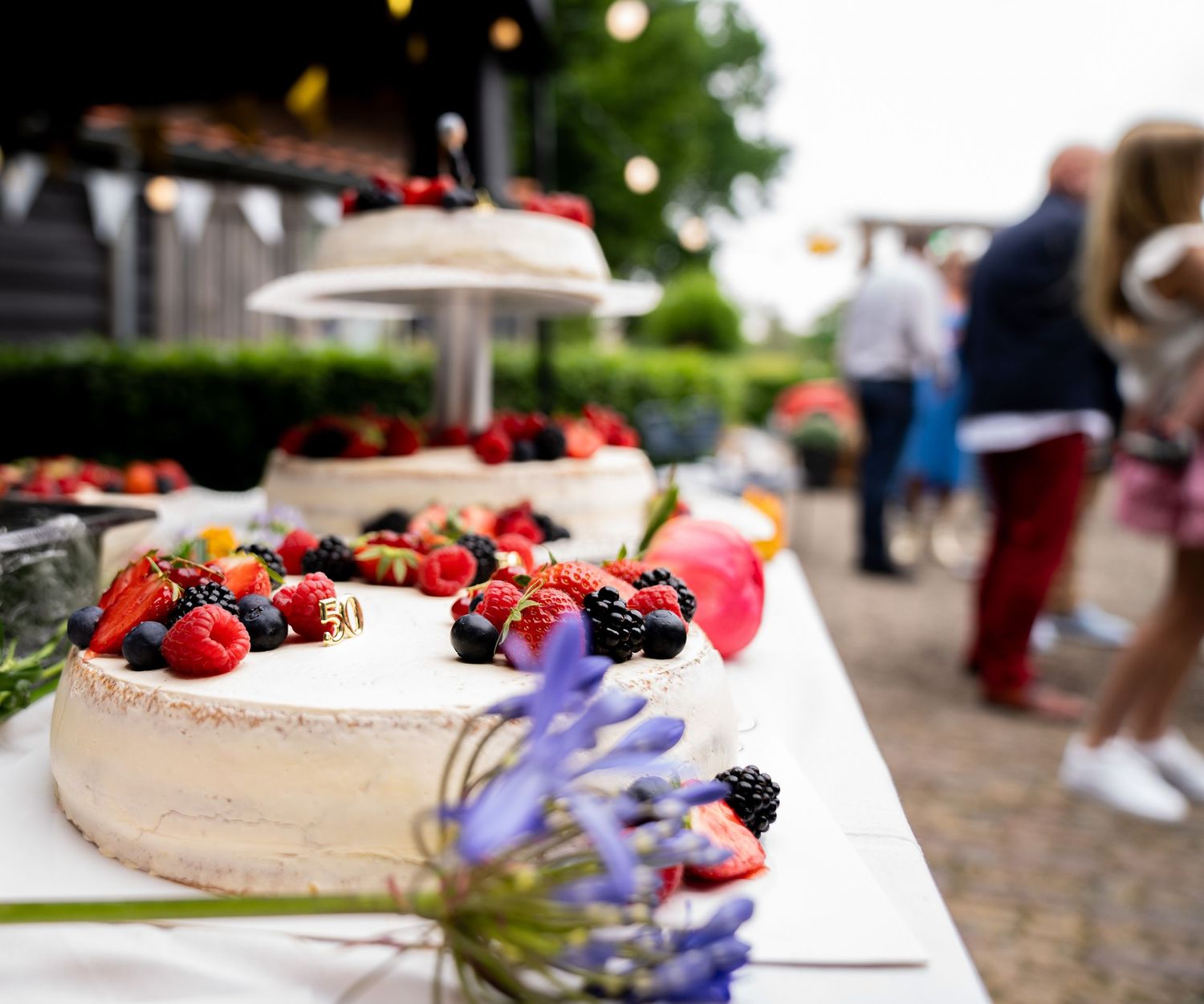 Een elegante desserttafel voor een bruiloft, met witte taarten gegarneerd met verse aardbeien en gemengde bessen, in een sfeervolle buitenom