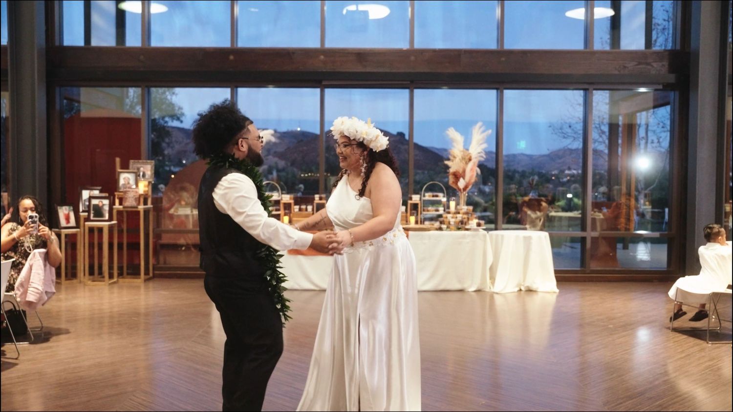 Two people dance together during a wedding reception in an elegant venue with mountain views through glass windows.