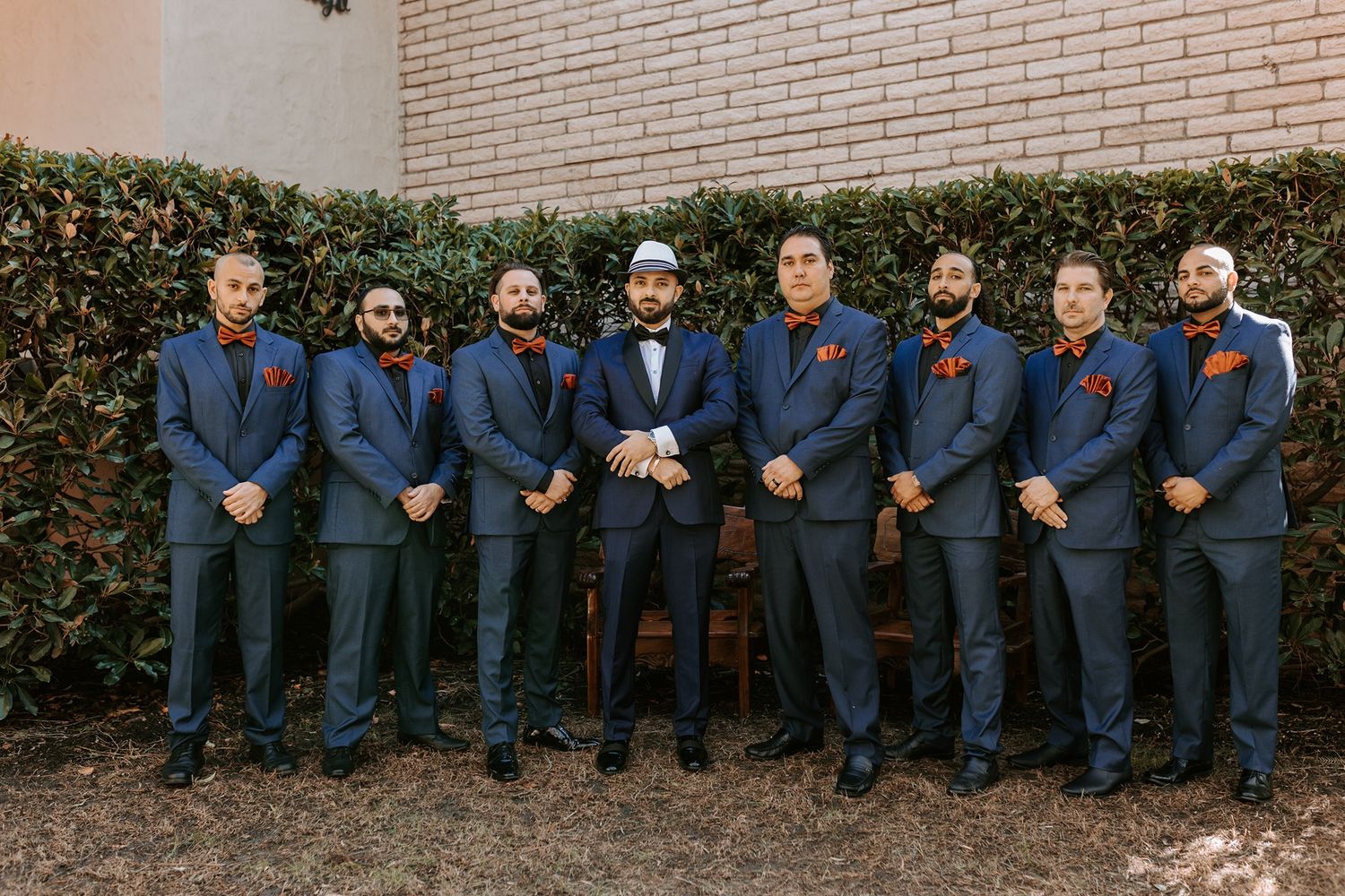 Groomsmen in navy suits sit casually on a brick wall during an outdoor wedding photoshoot at Rancho Bernardo Inn.