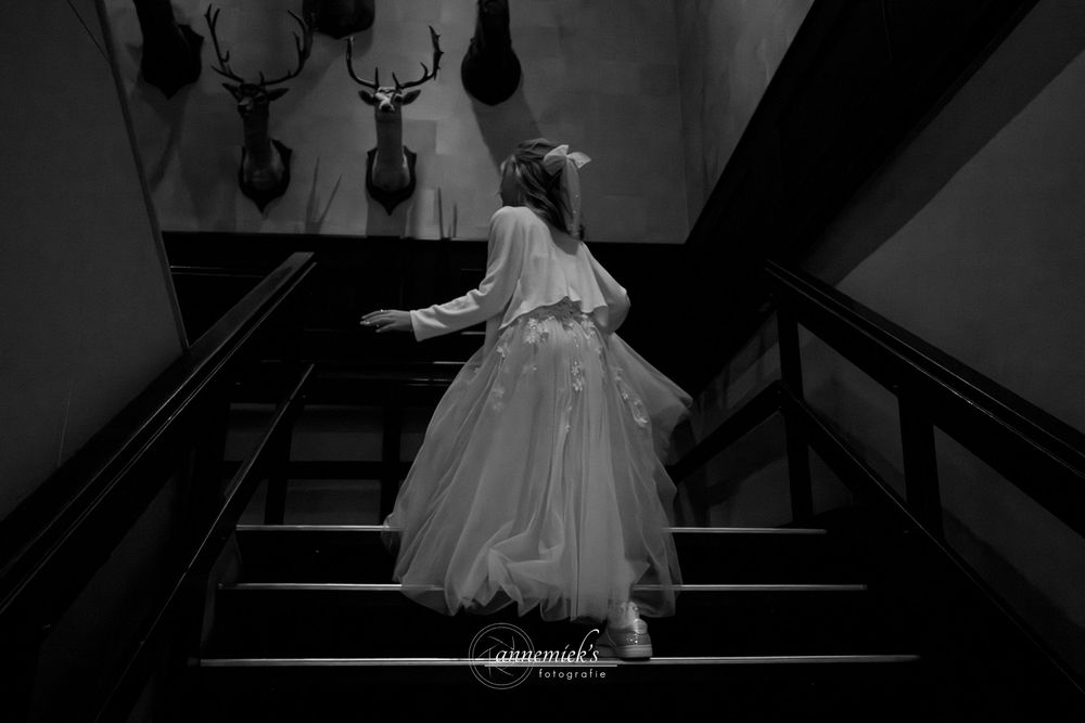 A graceful ballet dancer in a white tutu dress performs on dark stairs in a dramatic black and white photograph.