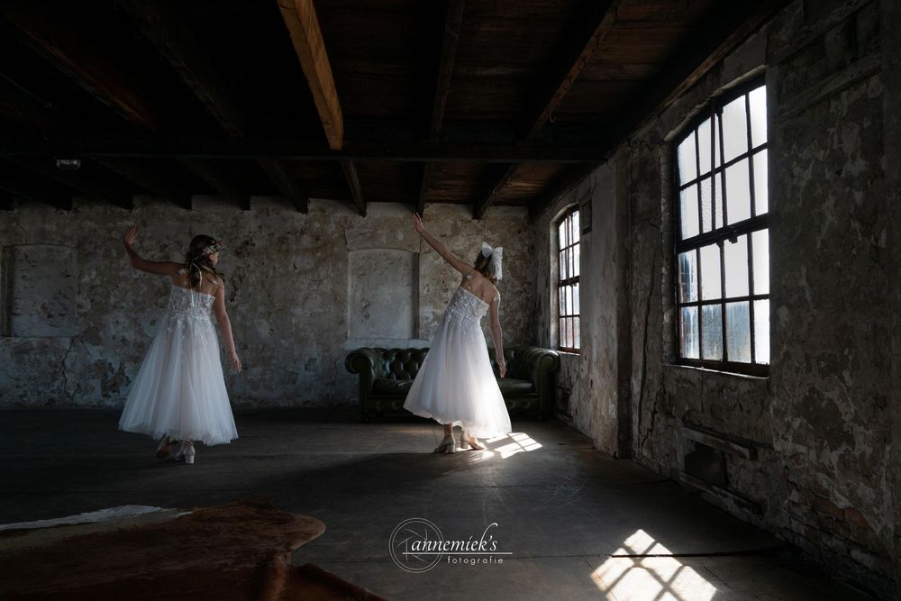 Two dancers in white tulle dresses perform in an atmospheric old stone building with dramatic window lighting.