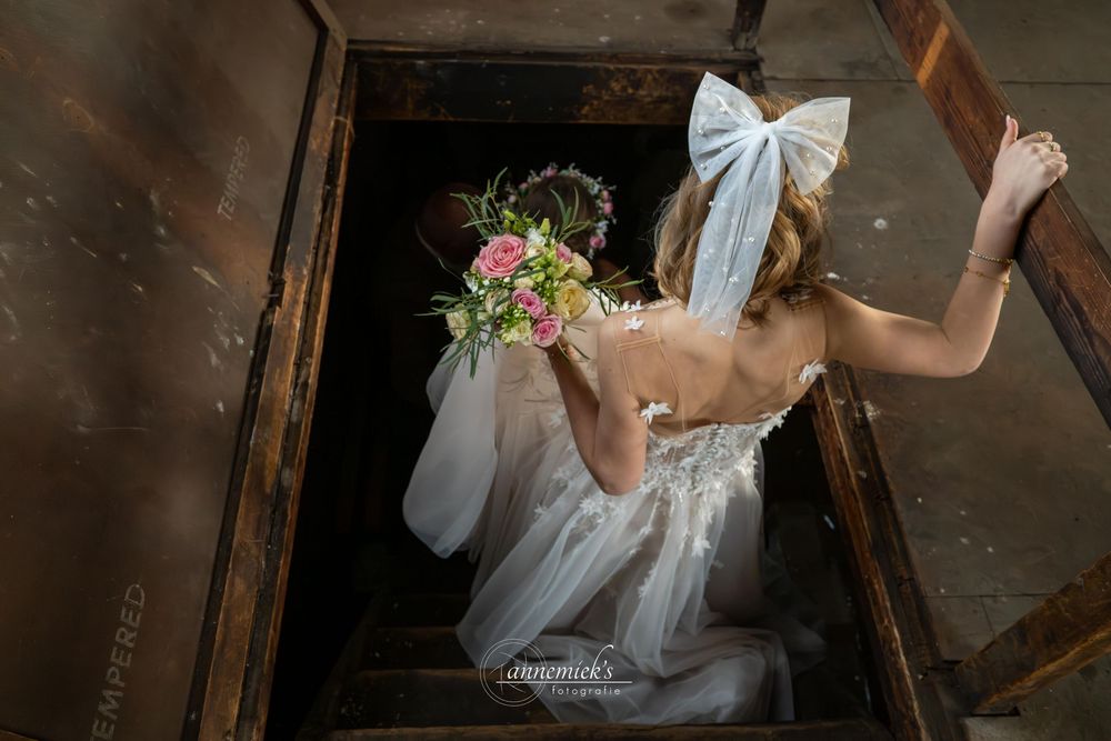 Elegant wedding couple descending wooden stairs in a rustic barn setting with soft natural lighting.