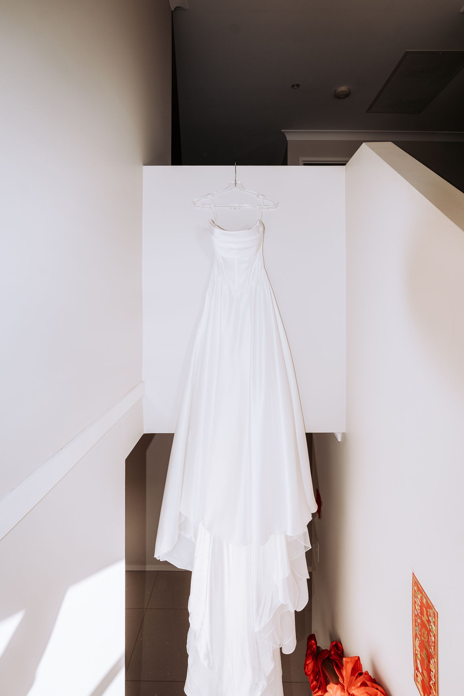 A white ghost costume with flowing fabric hangs against a wall, with a glimpse of orange decorations below.