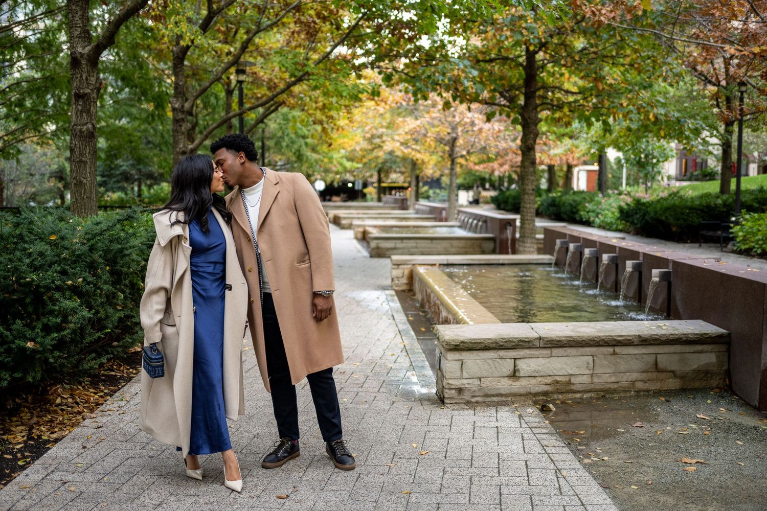 Two people walking together on a tree-lined path during autumn while having a conversation.