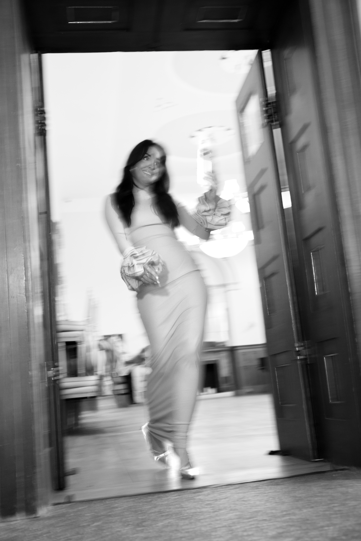 Blurred motion of people walking through a modern building corridor with reflective surfaces and bright lighting.