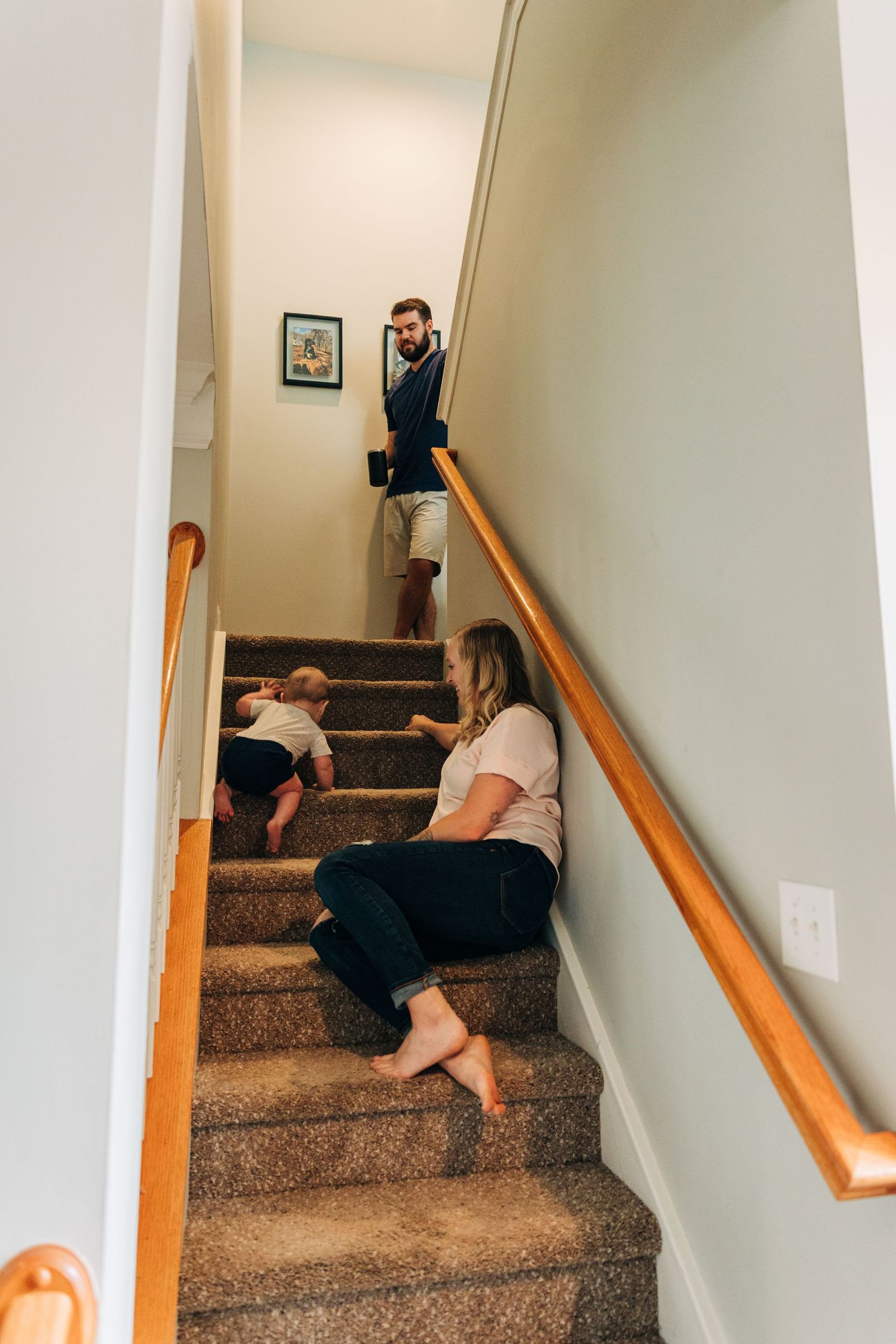 Family relaxing together on carpeted stairs inside home with wooden handrail and light colored walls.