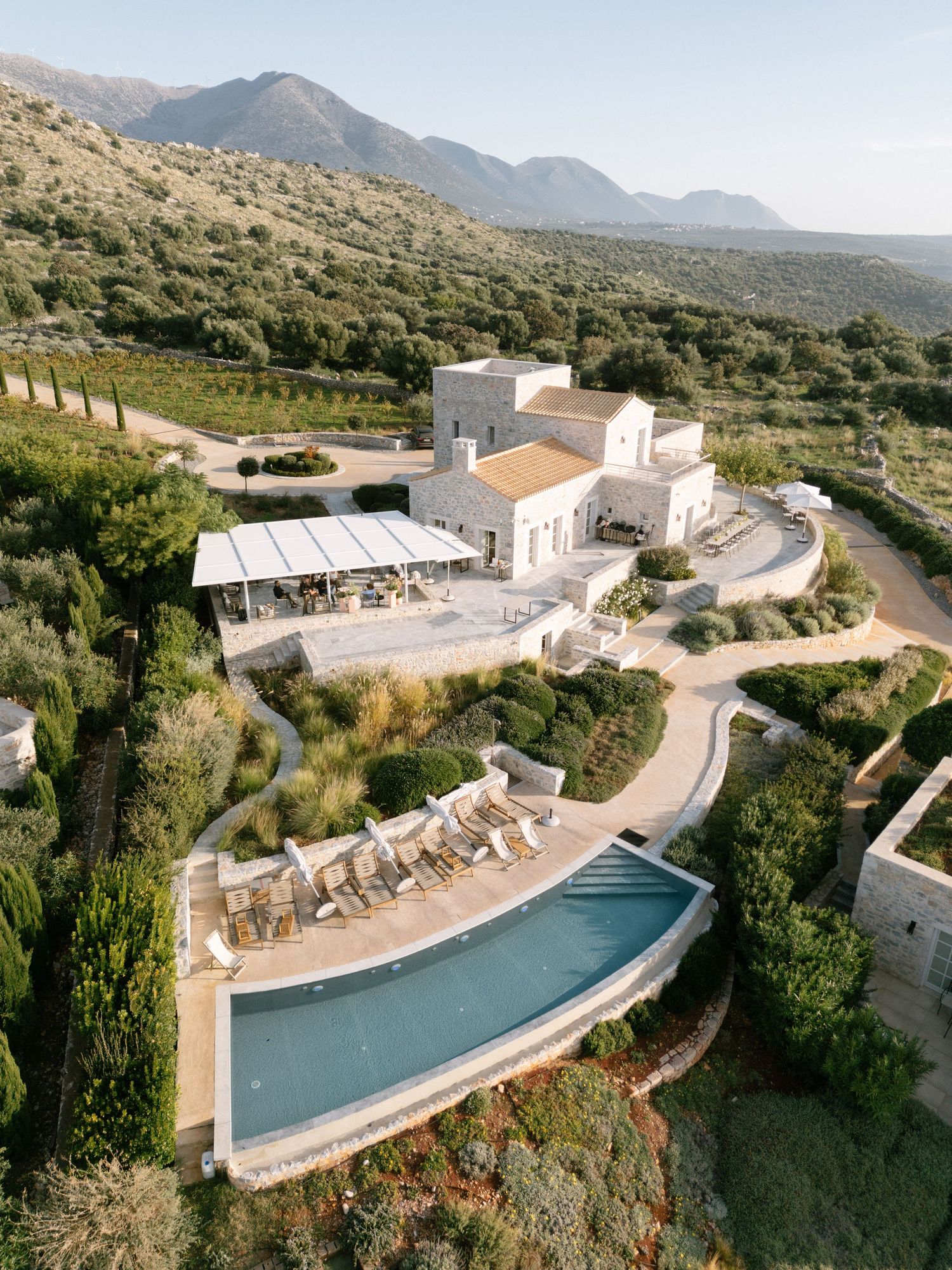 Aerial views of a luxurious hillside resort with curved infinity pools and white buildings nestled in mountainous terrain.