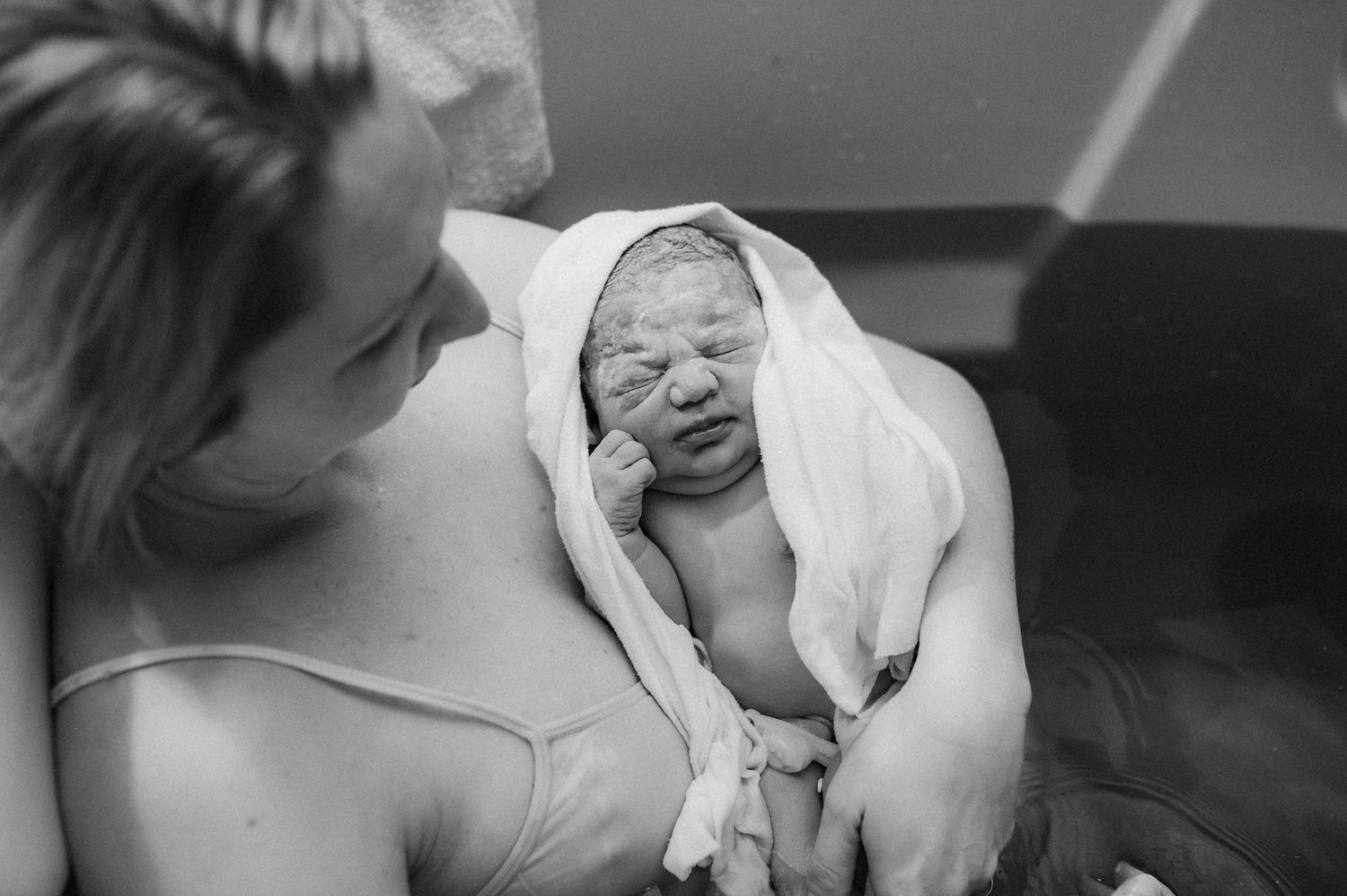 Black and white photo collage showing intimate moments between a parent and newborn baby in a hospital setting.