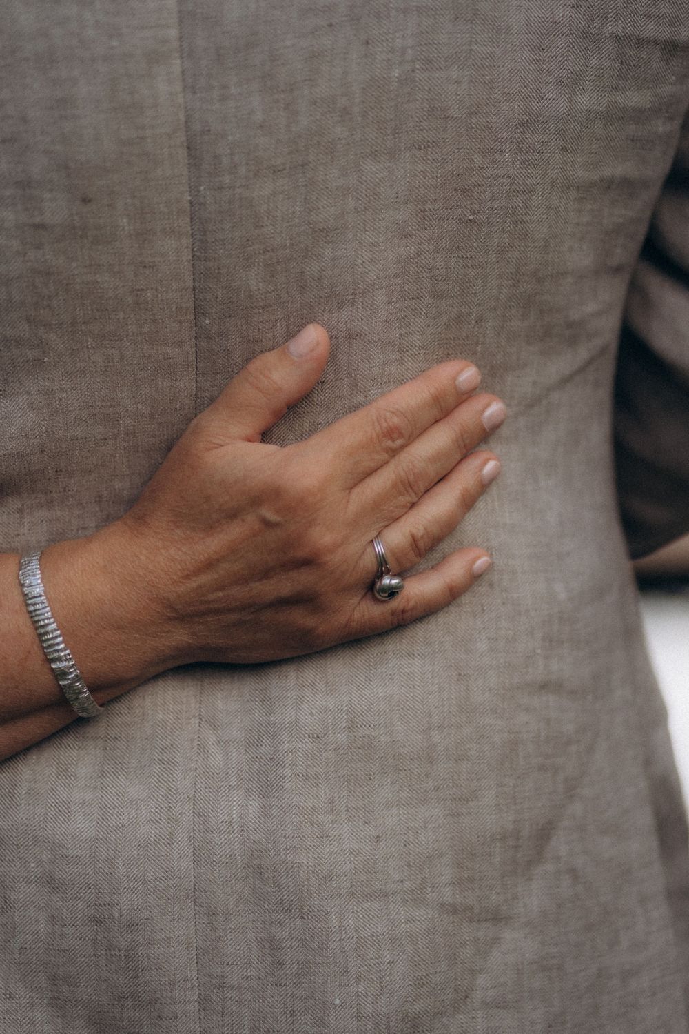 Close-up wedding photo of a hand with a ring resting on a grey suit