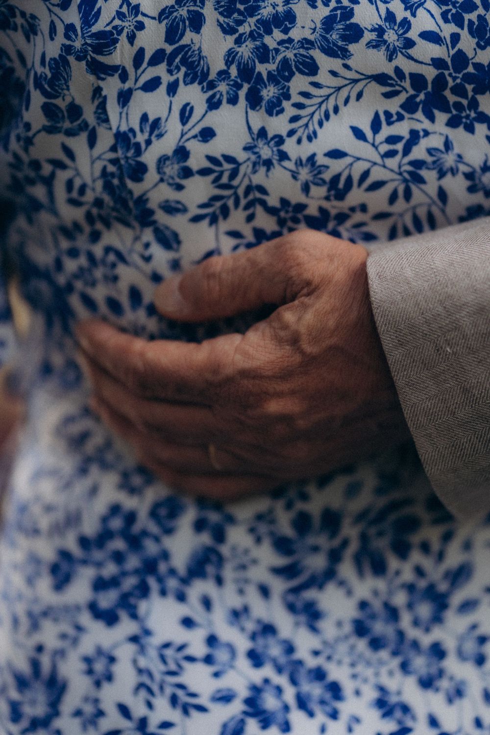 Close-up wedding photo of hands resting gently on a blue floral dress of the mother of the bride