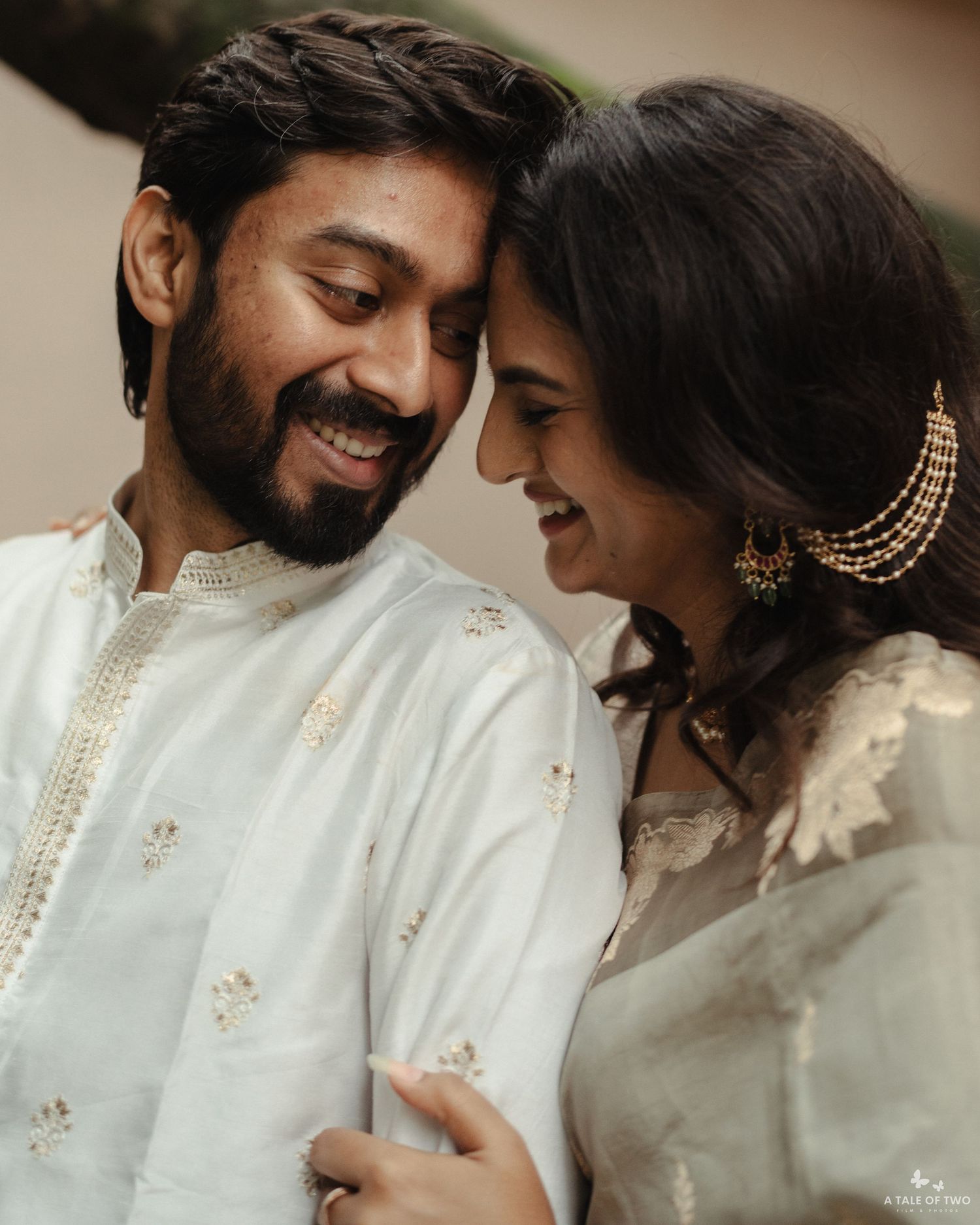 Smiling Indian couple in matching white kurta outfits share a tender close moment during wedding celebration.