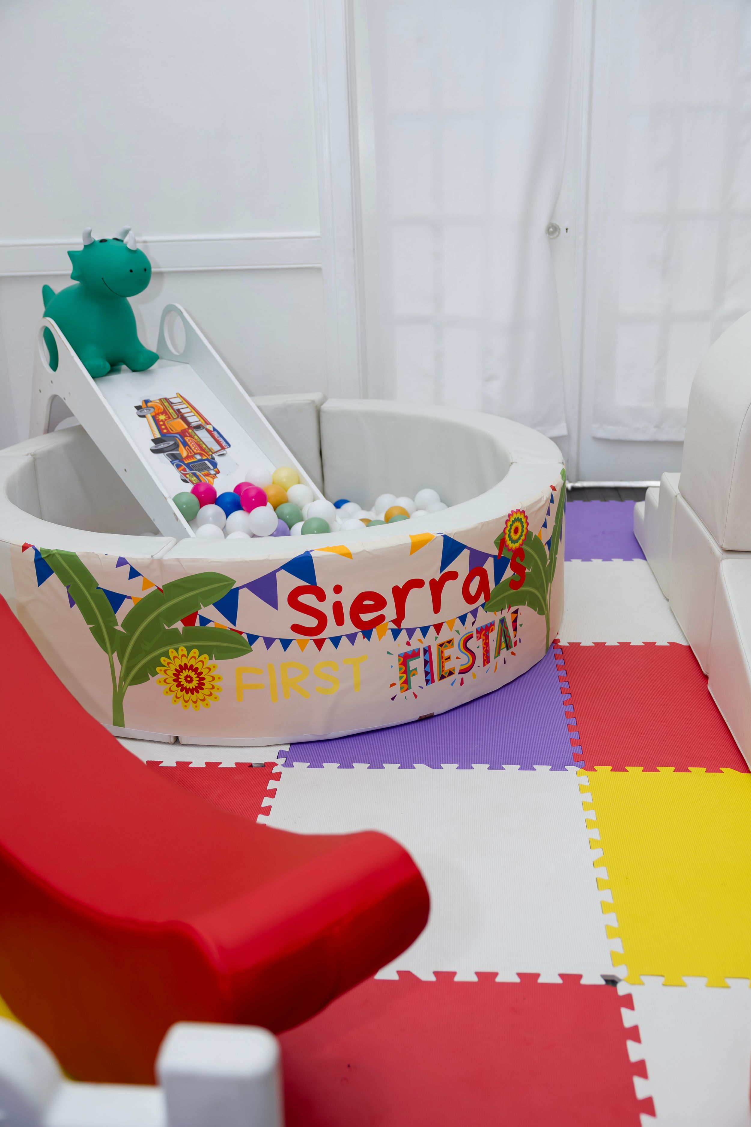 Colorful ball pit with slide reading Sierra's First Fiesta on foam play mats at a first birthday party.