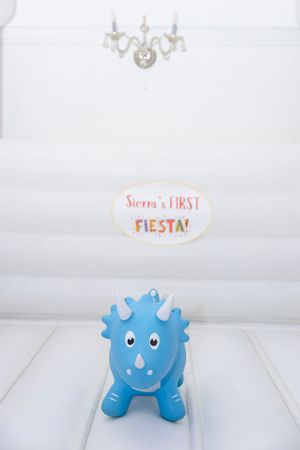 Blue triceratops toy dinosaur at Sierra's First Fiesta first birthday party with white bounce house backdrop.
