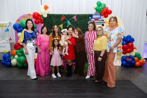 Group of people posing in colorful costumes at a festive party with balloon arch backdrop.