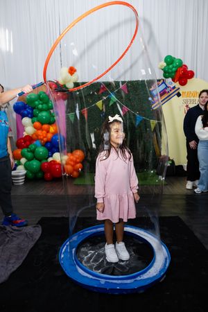 Young girl standing inside a giant soap bubble at a colorful fiesta-themed first birthday party.