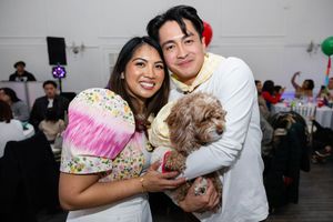 Smiling couple posing with an adorable brown curly-haired dog at a festive birthday party celebration.