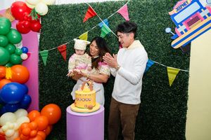 Parents celebrating with their baby girl during a cake smash at a colorful Filipino fiesta first birthday party.