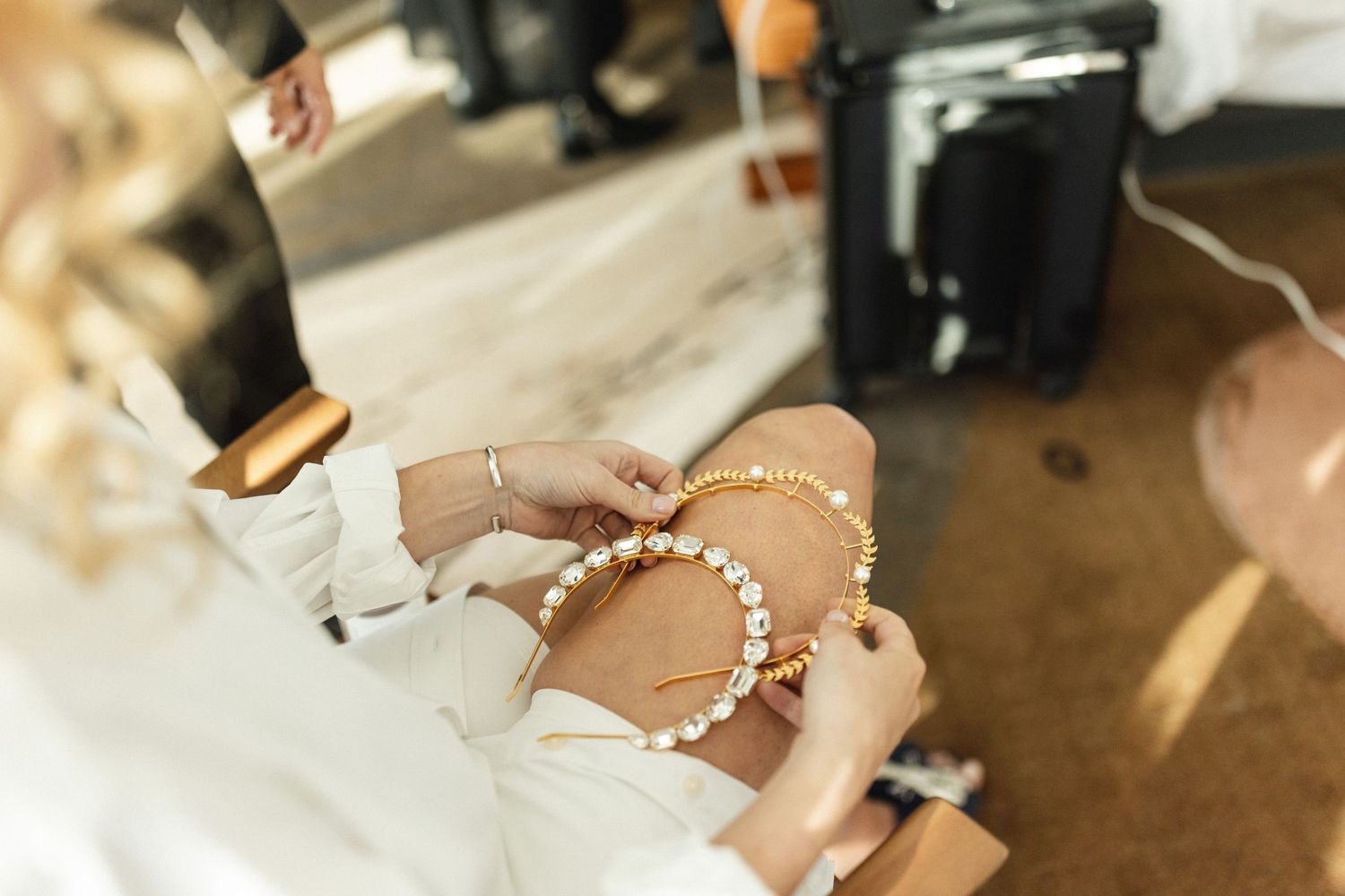 Close-up of hands holding gold and pearl bridal hair accessories during wedding preparations.