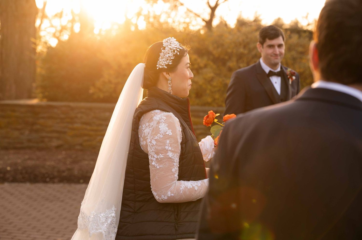 A wedding ceremony at sunset with warm golden light streaming through as the couple exchanges vows outdoors.