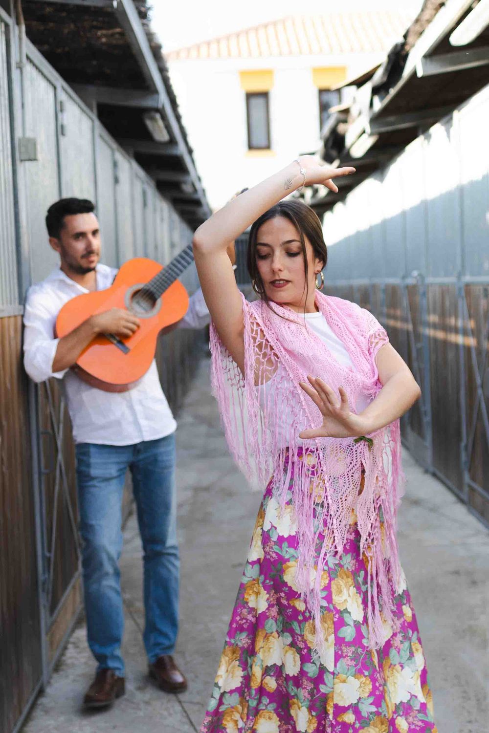 A flamenco dancer in a floral skirt and pink shawl performs while a guitarist plays in the background.