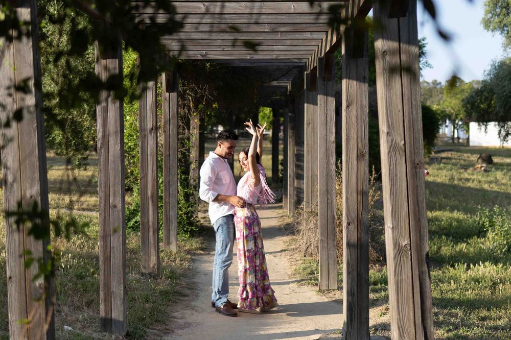 Couple dancing under a wooden pergola pathway surrounded by lush greenery in a romantic outdoor setting.