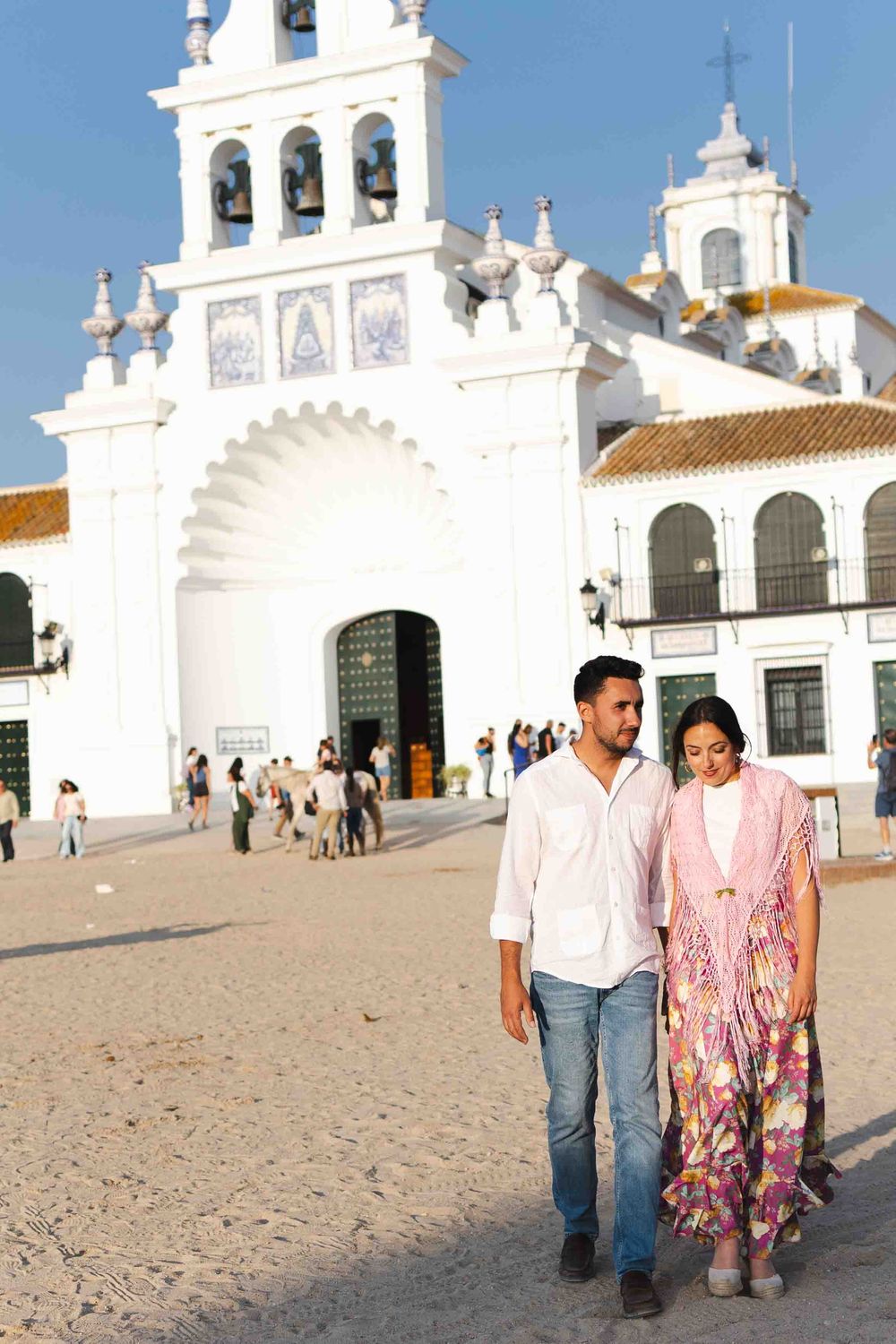 Couple walking hand in hand in front of a white Spanish church in El Rocio, Andalusia, Spain.