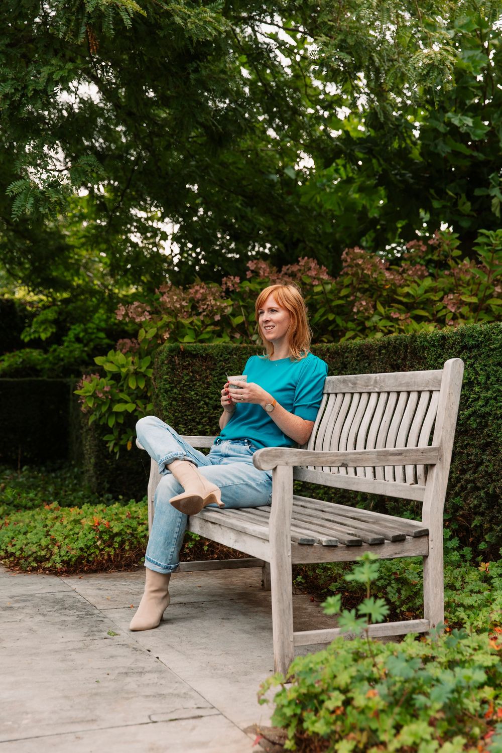 Person relaxing on white garden bench with coffee cup surrounded by greenery.