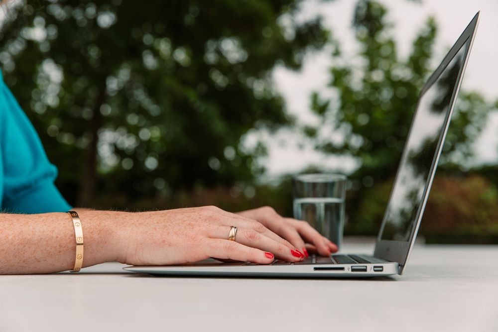 Close up of hands typing on laptop keyboard in outdoor setting.