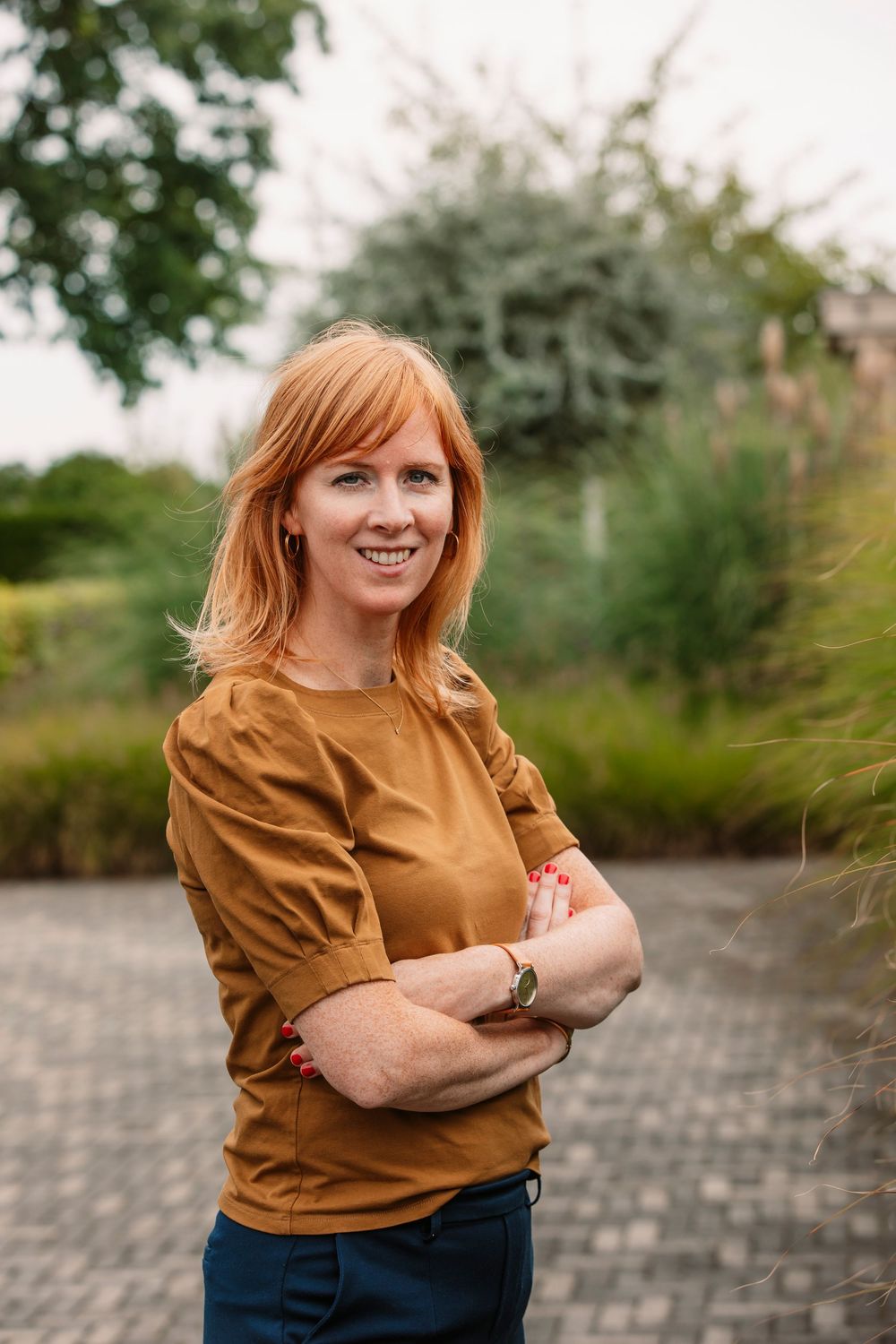 Person wearing brown top posing outdoors against natural background.