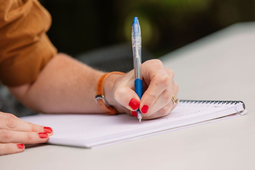 Close up of hands writing with pen in notebook with red nail polish.