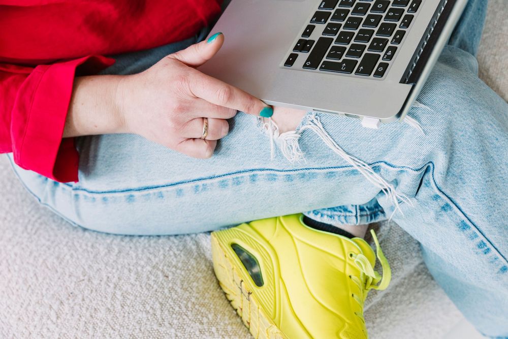 Laptop and hands wearing red sweater and light jeans shown from above.