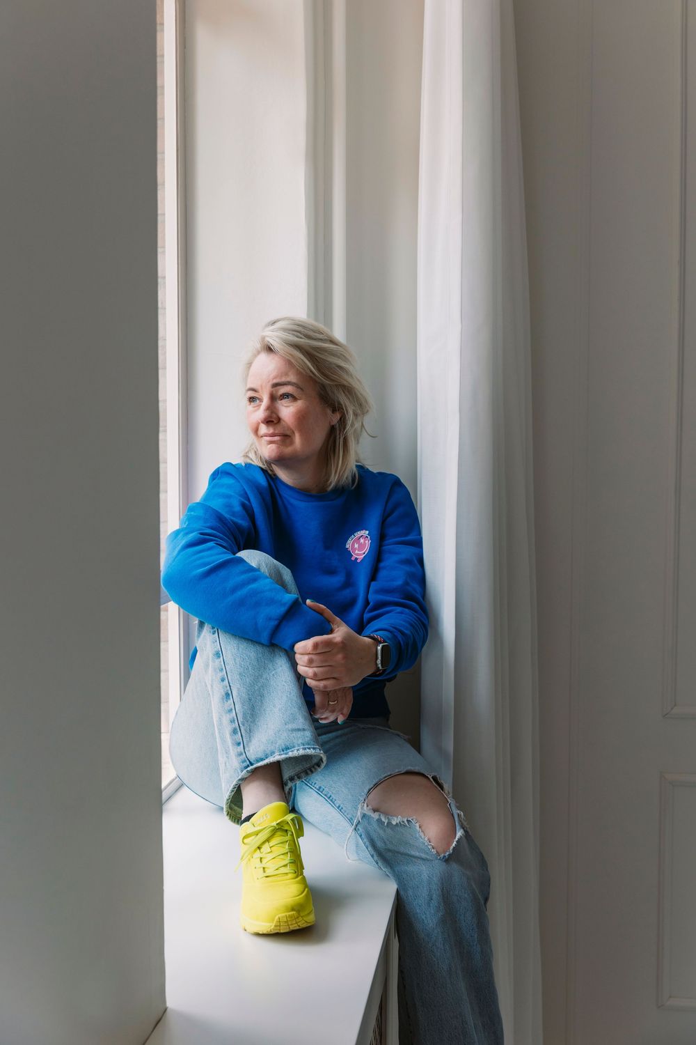Minimalist white interior with person wearing bright blue sweater and yellow shoes.