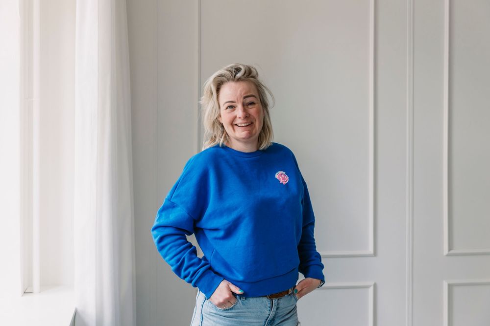 Person in royal blue sweater posing against white paneled wall.